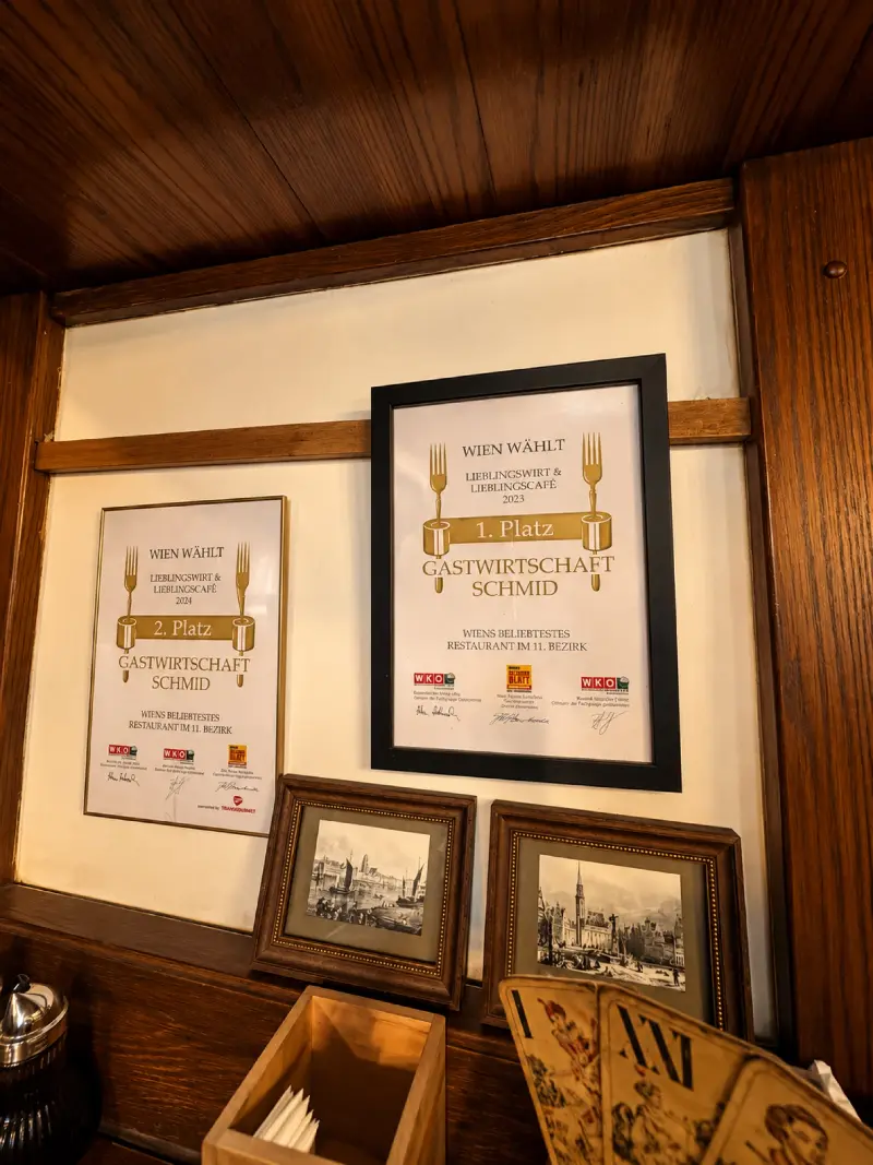 Zwei gerahmte Urkunden „Wien wählt Lieblingswirt & Lieblingscafé“ an der Holzwand der Gaststube