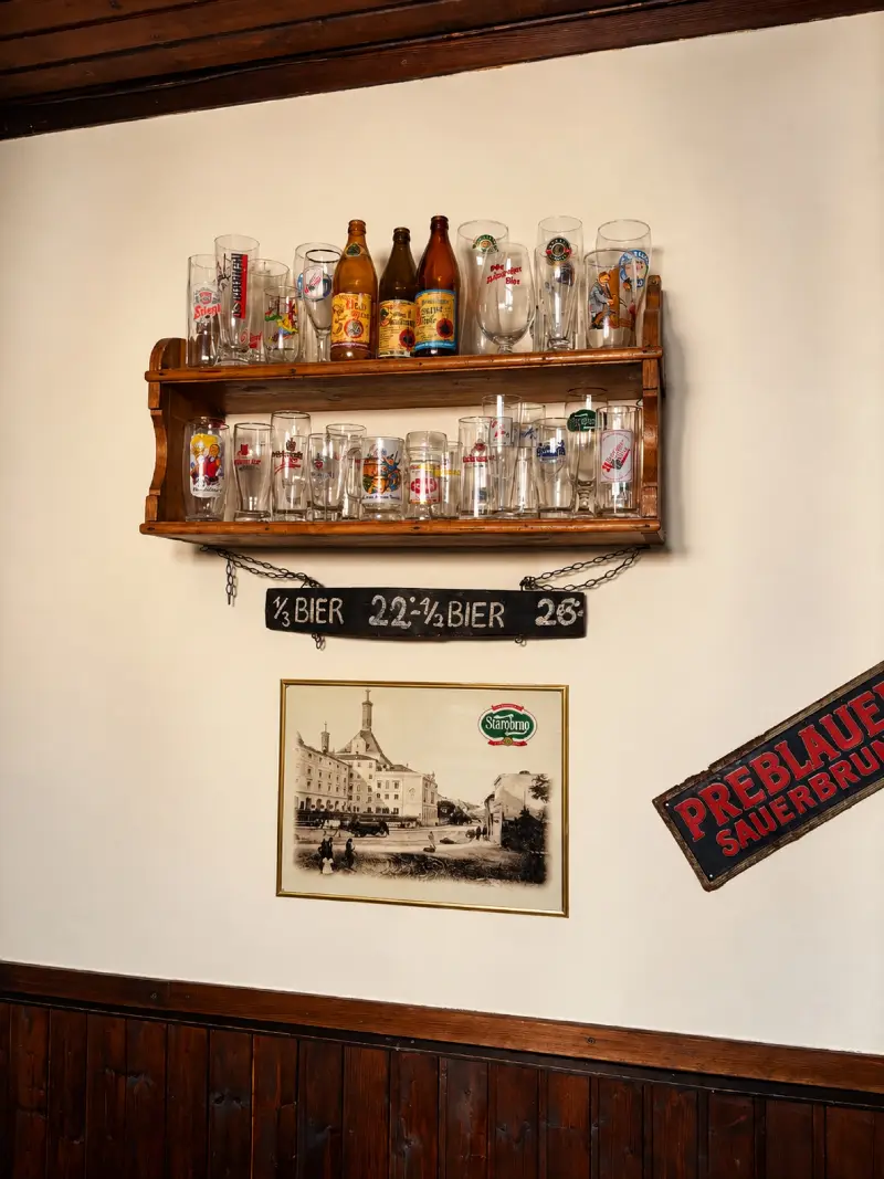 Alte Preistafel „⅓ Bier 22 · ½ Bier 26“ unter einem Regal mit Biergläsern früherer Brauereien