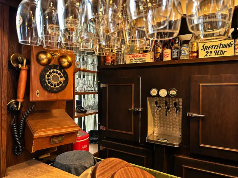Schank mit Wählscheibentelefon aus Holz, Gläserbord und dem Schild „Sperrstunde 22 Uhr“