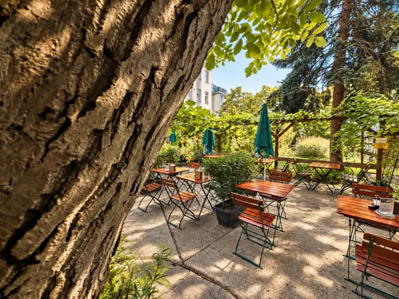 Der alte Nussbaum im Gastgarten, davor Tische mit grünem Sonnenschirm