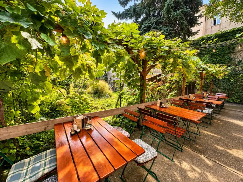 Lange Tische und Bänke auf der Terrasse unter der Weinlaube