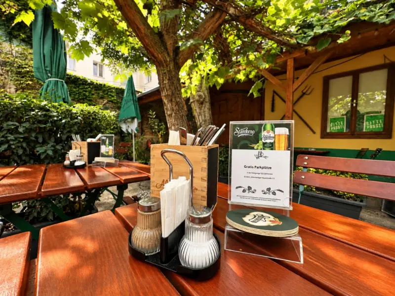 Gedeckter Tisch im Gastgarten, im Hintergrund Sonnenschirme und die Gartenhütte