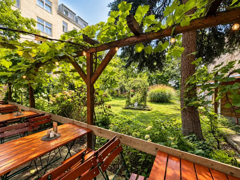 Weinlaube über den Tischen im Gastgarten, dahinter die Rasenfläche des Innenhofs