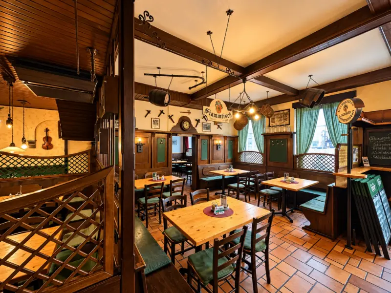 Blick durch die Gaststube mit Holzdecke, gedeckten Tischen und der Tafel an der Wand